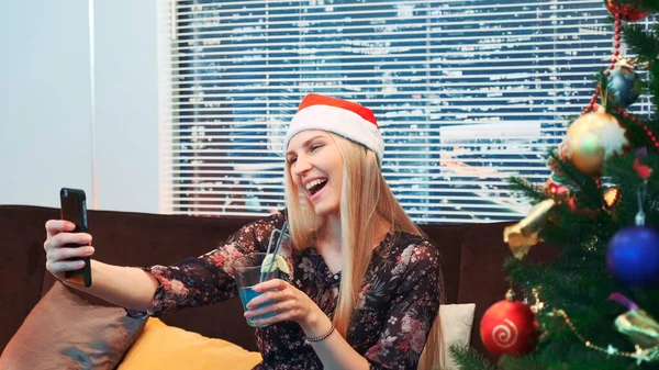 Vue latérale de belle femme faisant selfie dans le chapeau de Père Noël et avec boisson dans ses mains — Photo