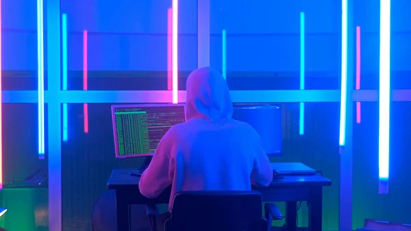 Medium back view shot of criminal hacker working in the evening on computer in big office