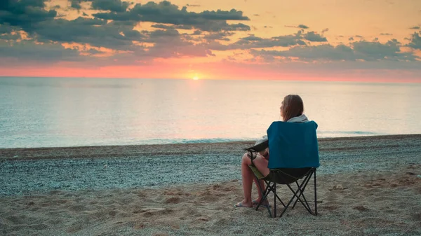 Žena obdivuje západ slunce na moři sedí v skládací turistické křeslo — Stock fotografie