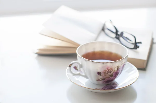 Kopje thee, oud boek en glazen — Stockfoto