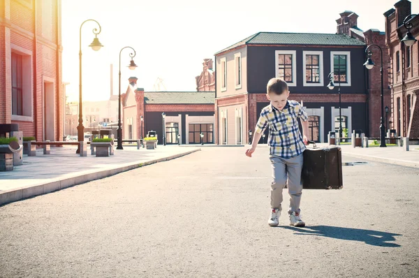 Little kid is holding the suitcase and walking down the sunny st — Stock Photo, Image