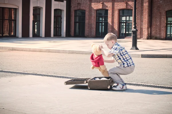 Little kid is opening the suitcase on the sunny street — Stock Photo, Image