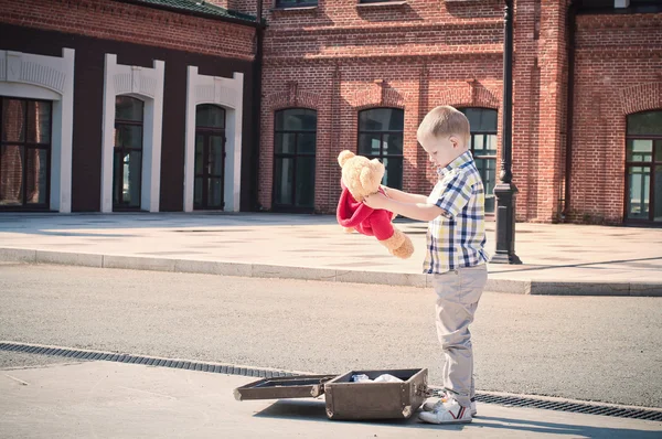 Liten unge öppnar resväska och med nallebjörn leksaken på — Stockfoto