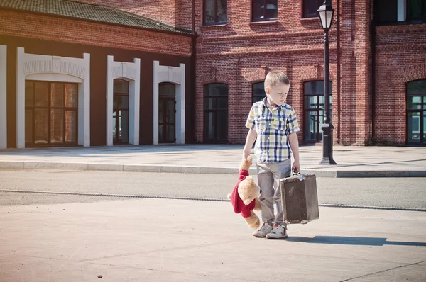 Little kid is holding the suitcase and teddy bear toy and walkin — Stock Photo, Image