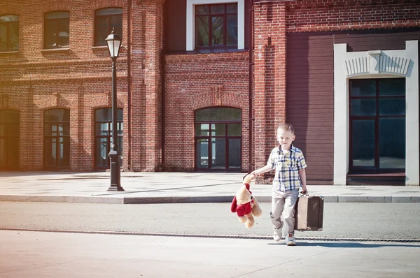 Niño pequeño con maleta y juguete de oso de peluche cruzando el soleado s — Foto de Stock