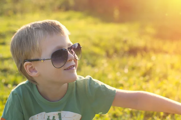 Ładny ładny dziecko w okulary siedzi na zielonej trawie w — Zdjęcie stockowe