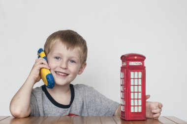 Telefon ve kırmızı telefon kulübesi üzerinde konuşurken çocuk