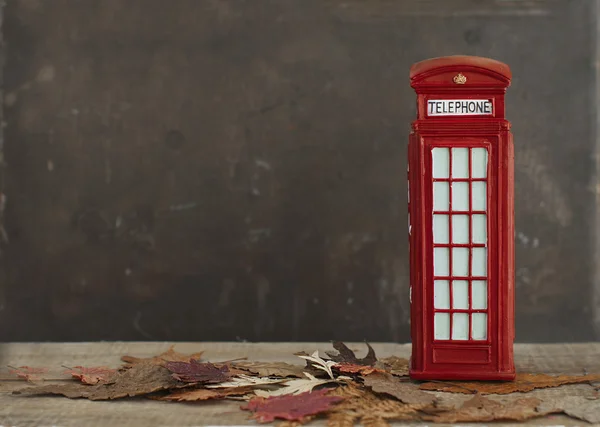 Autumnal image with dry maple leaves and red british phone booth — Stock Photo, Image