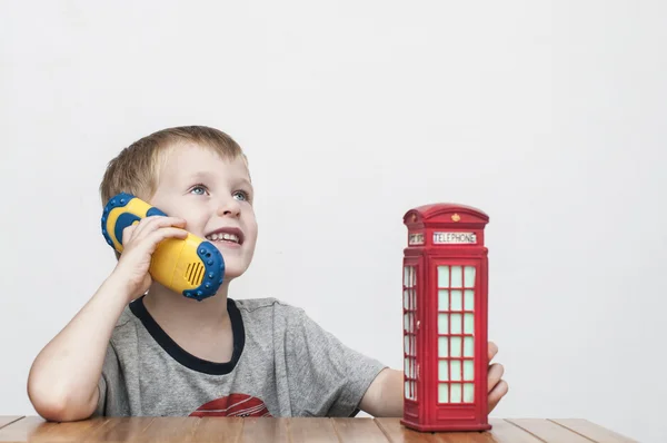 Menino falando no telefone e na cabine telefônica vermelha — Fotografia de Stock