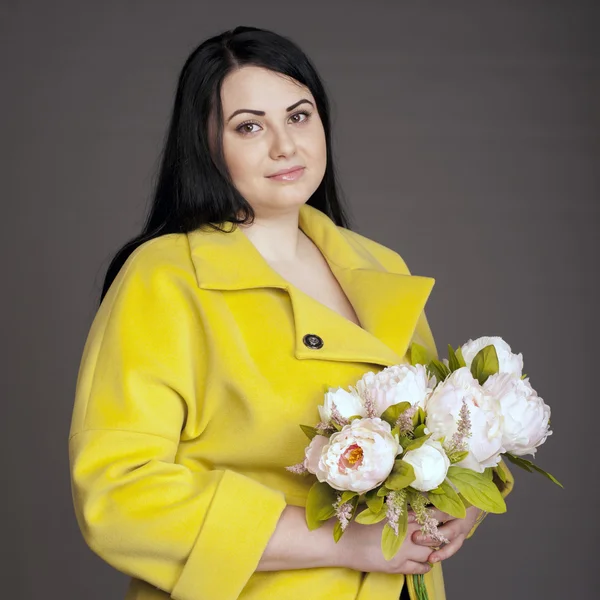 Morena corpulenta em um casaco amarelo com um buquê de flores — Fotografia de Stock
