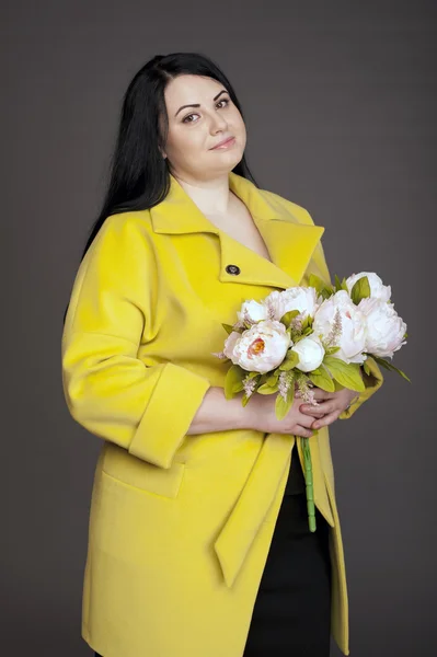 Corpulent brunette in  in a yellow coat with a bouquet of flowers — Φωτογραφία Αρχείου