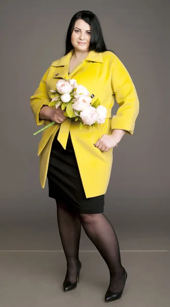 Corpulent brunette in  in a yellow coat with a bouquet of flowers — Stock fotografie