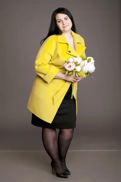 Corpulent brunette in  in a yellow coat with a bouquet of flowers — Stock Fotó