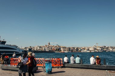 İSTANBUL, TÜRKEYE - 12 Kasım 2020: Kıyı şeridinde, arka planda deniz ve binaları olan insanlar 