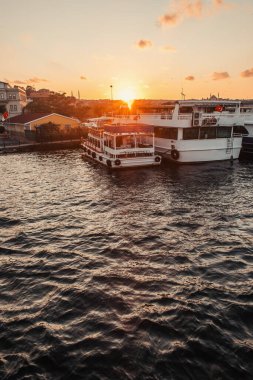 Kentin kıyısındaki binalar yakınlarındaki demirlemiş botlar ve arka planda gün batımı gökyüzü, İstanbul ve Türkiye 