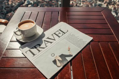 Kafedeki ahşap masada bir fincan kahve ve seyahat gazetesi. 