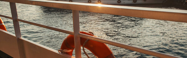 Lifebuoy on railing of ship with sea at background, banner 