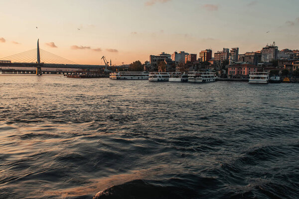 Корабли пришвартованы рядом с набережной с мостом метро Golden Horn и Стамбулом на заднем плане во время заката, Турция 
