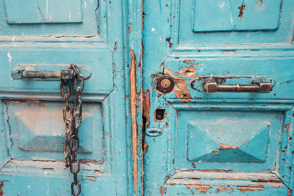 old wooden doors, with blue cracked paint, rusty metallic handles and chain 