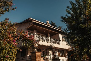 İki katlı villa, yeşil ağaçların yanında.