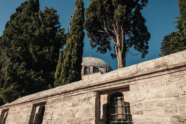 Каменная стена с огороженными окнами и высокими деревьями возле мечети Михрима Султан, Стамбул, Турция — стоковое фото