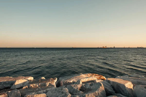 Sonnenlicht auf Steinen am Meer und wolkenloser Himmel über der Skyline — Stockfoto