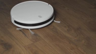 Beyaz robotik süpürge, oturma odasının iç kısmındaki toz temizleme kabını kaplıyor..