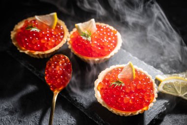 Siyah arka planda servis edilen kırmızı havyarlı turtalar. Lezzetli deniz ürünleri. Buhar ve sert ışık