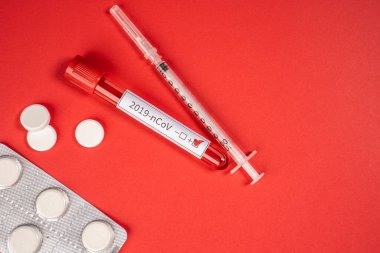 Roman Coronavirus - 2019-NCoV. Kırmızı zemin üzerinde 2019 nCoV Coronavirus tarafından tanımlanmış kan olan test tüpü. Virüsü tedavi etmek için şırınga ve ilaçlar.