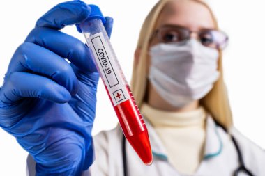 Beyaz kadın sağlık çalışanı, laboratuvar önlüğü, yüz maskesi ve Coronavirus 'a karşı ameliyat eldiveni takıyor.