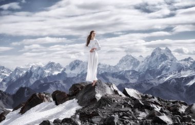Beyaz elbiseli ve yalın ayaklı bir model, karlı dağ zirvelerinin zeminini yalayıp yutar.