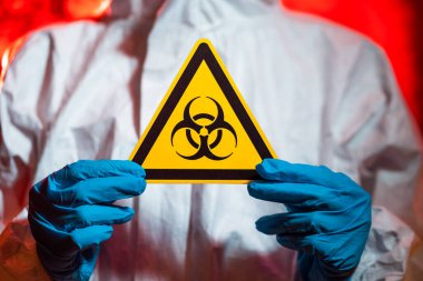 Koruyucu kıyafetli bir doktor biyolojik tehlike işareti taşıyor. Coronavirus salgını konsepti, karantina