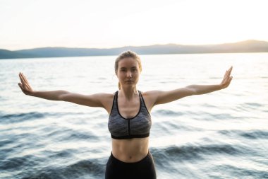 Genç ve güzel kadın vücut geliştirici poz veriyor ve gölde kaslarını gösteriyor.