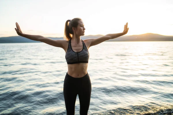 Çekici genç bir kadın denge için yoga yapıyor ve göl kenarında geriniyor.