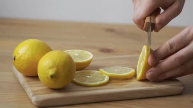 Dişi eller, limonu bıçakla kesip tahta kesme tahtasıyla yuvarlak dilimlere ayırıyor.