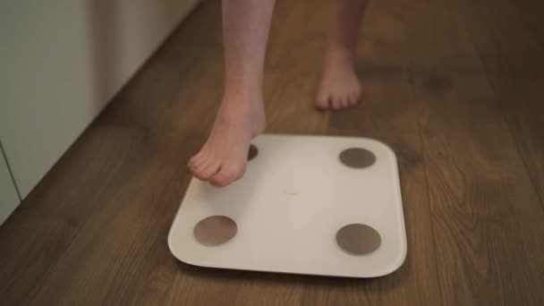 Eine Frau zu Hause bringt ihre Füße auf die Waage, um ihr Gewicht zu messen — Stockvideo