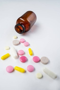 Beyaz arka planda bir konteynırdan dökülen haplar