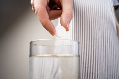 Cam şeffaf bir bardağa atılan köpüklü tablet, cam masanın üzerinde.