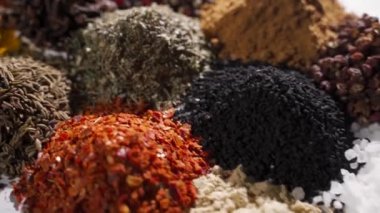 Bitki yığınları baharat tozları doğal ve sağlıklı kokulu kokulu tohumlar, tohumlar beyaz masada birbirinden ayrı yatar. Dolly çekim yapar Kamera baharatlar arasında hareket eder