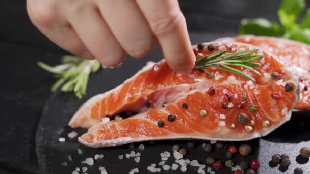 Un cuoco mette un rametto di rosmarino su una bistecca di salmone.Pesce rosso salmone crudo con pepe e sale. — Video Stock