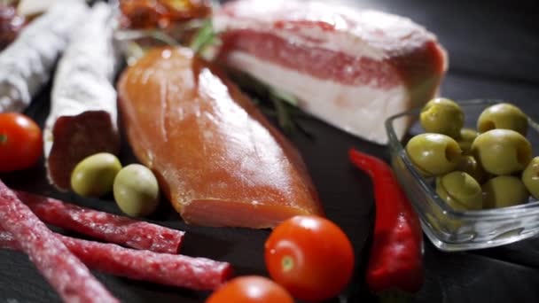 Geassorteerde delicatessen, ham, salami, spek en tomaten op het zwarte stenen dienblad — Stockvideo