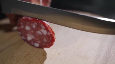 Profesyonel bir mutfakta deneyimli bir şef baharatlı İtalyan salam sosisini çok ince dilimlerle profesyonel bir bıçakla keser..