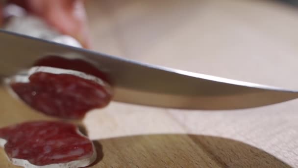 プロのキッチンで経験豊富なシェフが熟練したイタリアのサラミソーセージを非常に薄いスライスでプロのナイフでカットします。. — ストック動画
