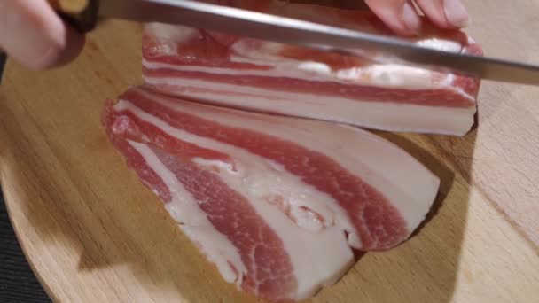 Chef cuts pieces of raw bacon by sharp knife on the wooden board — Stock Video