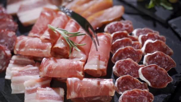 Assorted deli meats, ham, salami, bacon and tomatoes on the black stone tray — Stock Video