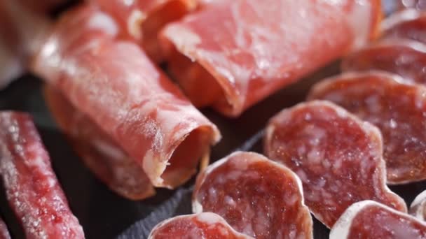 Geassorteerde delicatessen, ham, salami, spek en tomaten op het zwarte stenen dienblad — Stockvideo