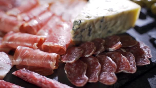 Geassorteerde delicatessen, ham, salami, spek en tomaten op het zwarte stenen dienblad — Stockvideo