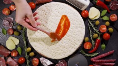 Şef pizza restoranında pizza hamuruna domates sosu sürüyor.