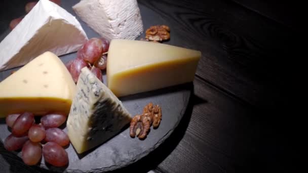 Un assortiment d'entrées de vin, d'entrées ou de dîners gastronomiques. Vue de dessus, à proximité, un coin de fromage, sur une assiette en bois rare, dégustation de vin français. — Video