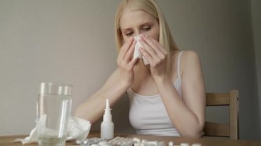 Karantina sırasında mutfakta genç bir kadın. Masada oturan ve hapşıran kız. Burun akışı ve hastalıktan muzdarip..